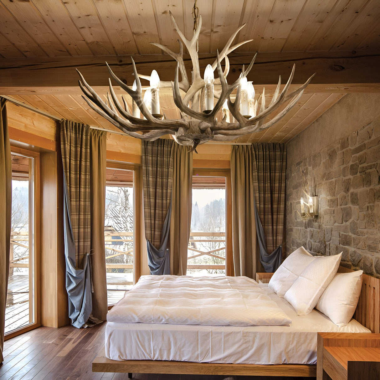 A cozy bedroom with a rustic design features a large wooden bed with white bedding, a stone accent wall, and the Flow 8 Light Chandelier in dark brown. The room has three large windows offering views of a winter landscape, complemented by wooden ceilings and flooring.