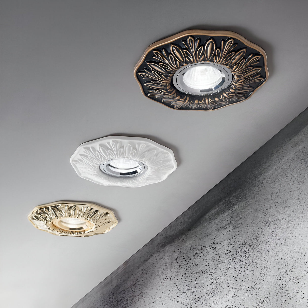 The ceiling showcases three elegant recessed Olivia downlights, each adorned with decorative floral-patterned frames available in black, white, and gold. The ceiling is angled, and the background has a textured gray finish, enhancing the modern interior design.