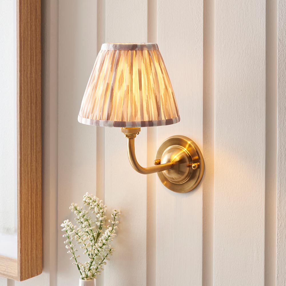 Endon Brackdale Ikat wall light with brushed aged brass curved arm and natural Ikat printed faux silk shade, mounted on a panelled hallway wall.
