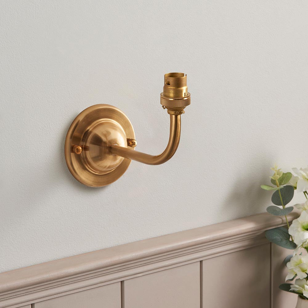 Endon Brackdale Ikat wall light in brushed aged brass, showing the domed backplate, curved arm and B22 lamp holder mounted above panelled wainscoting.