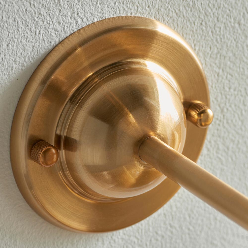 Close-up of the Endon Brackdale Ikat wall light's brushed aged brass dome and curved arm, fixed to a textured off-white wall.