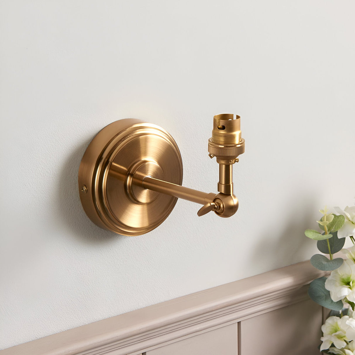 Endon Corven wall light in brushed aged brass with stepped backplate, adjustable knuckle arm and B22 lamp holder, mounted on a pale wall.