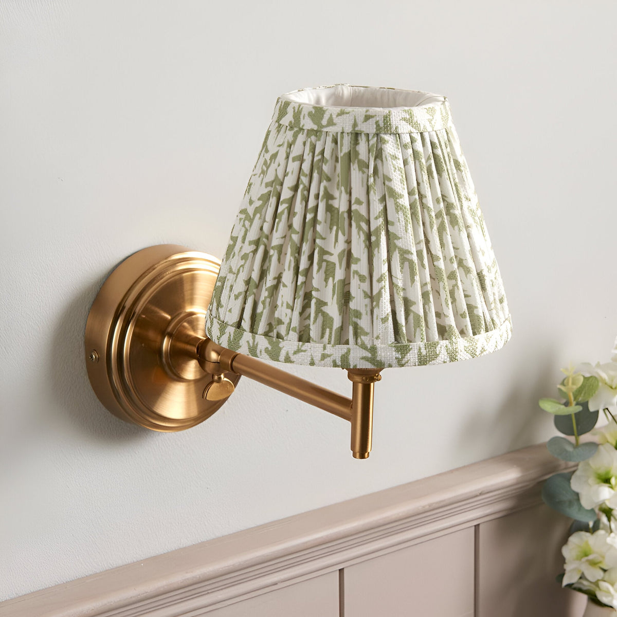 Cliffwood Leaf Wall Light in brushed brass with an adjustable knuckle arm and pleated green leaf-print fabric shade, mounted on a light grey wall.