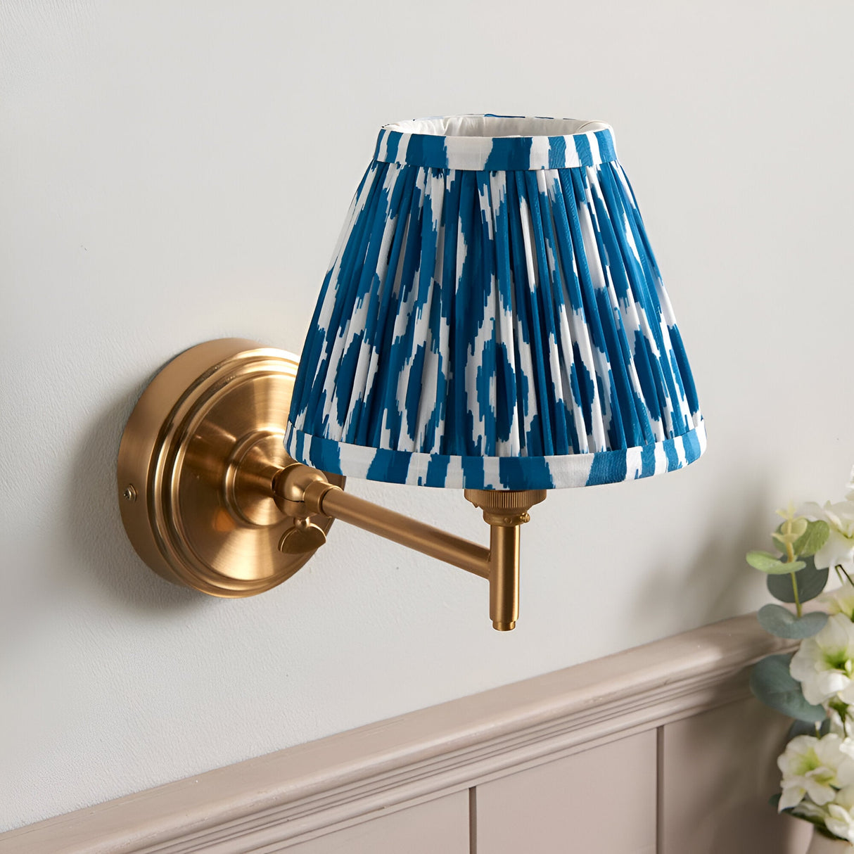 Cliffwood Ikat Wall Light in brushed brass with an adjustable knuckle arm and pleated blue and white Ikat-print fabric shade, mounted on a light grey wall.