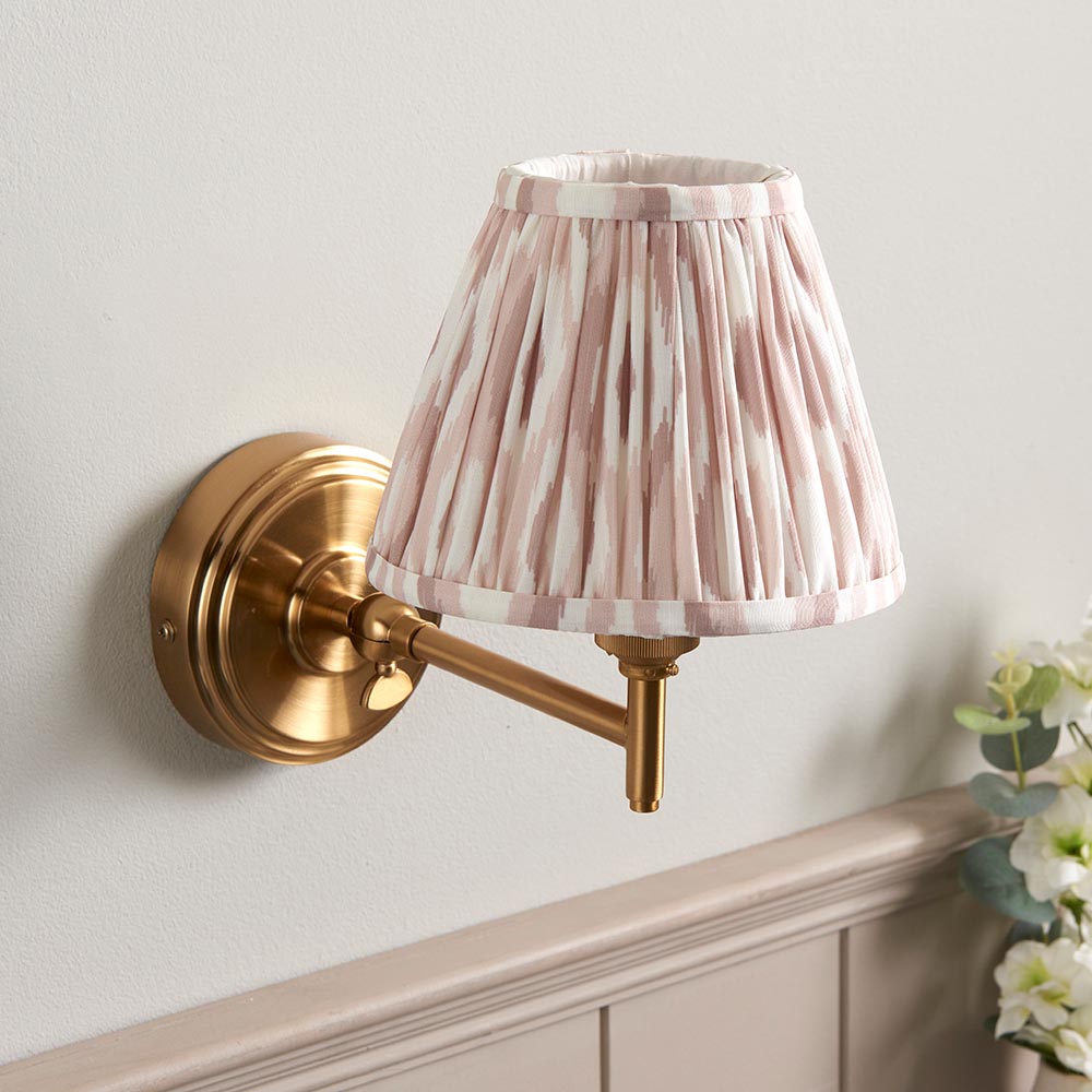 Cliffwood Ikat Wall Light with brass adjustable arm and pleated pink-and-white patterned fabric shade, mounted on a light grey wall.