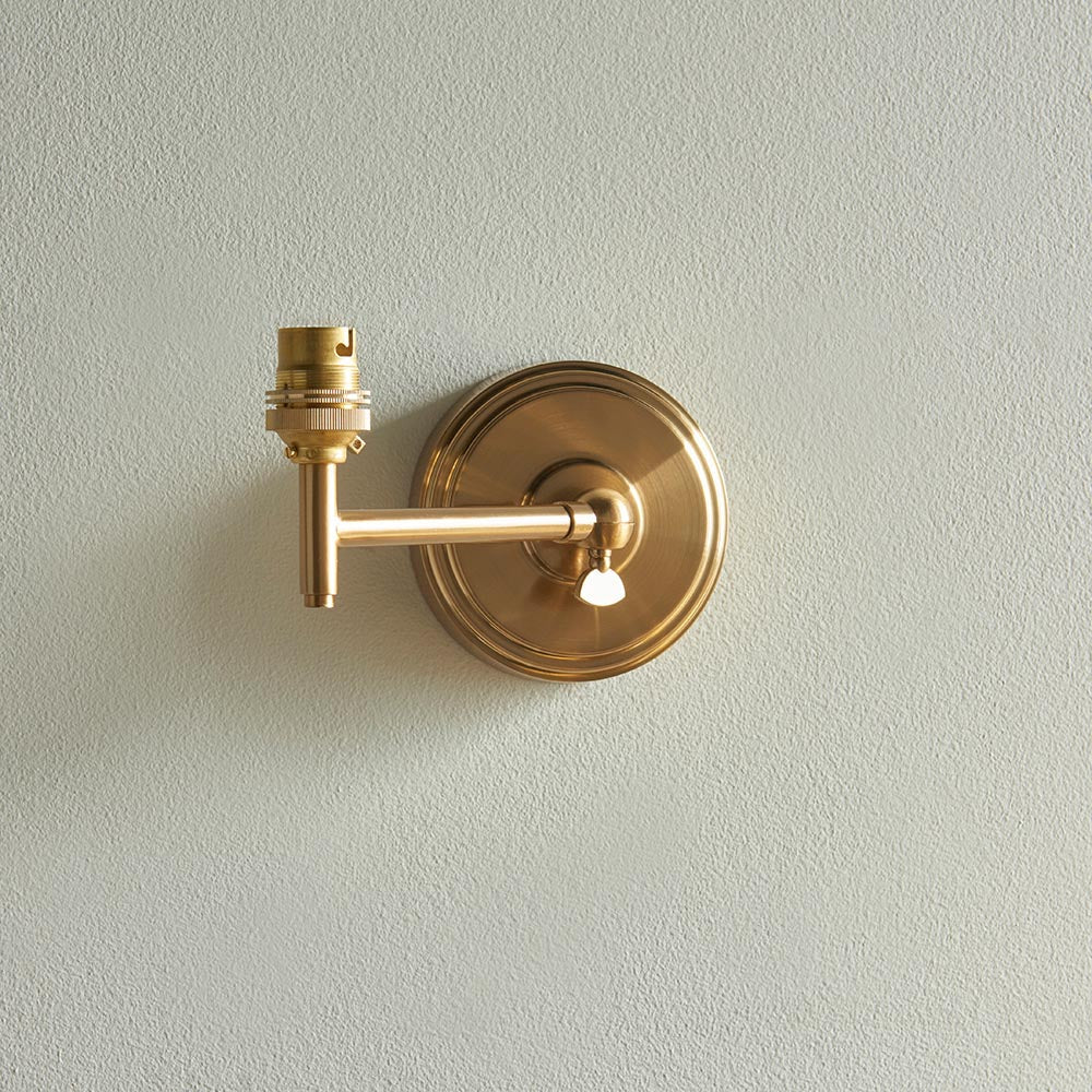 Cliffwood Ikat wall light in brushed aged brass with an adjustable knuckle arm and B22 lamp holder, shown without shade on a plain grey background.