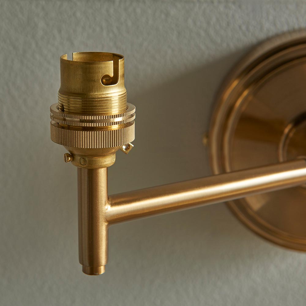 Close-up of the Cliffwood wall light's brass B22 lamp holder and adjustable knuckle arm, shown without shade against a plain grey wall.