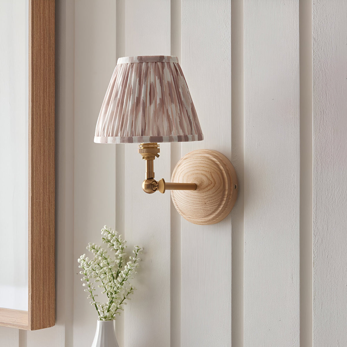 Endon Danemere Ikat wall light with natural ash wood back plate, brushed aged brass arm and pleated cream Ikat tapered shade on panelled wall.