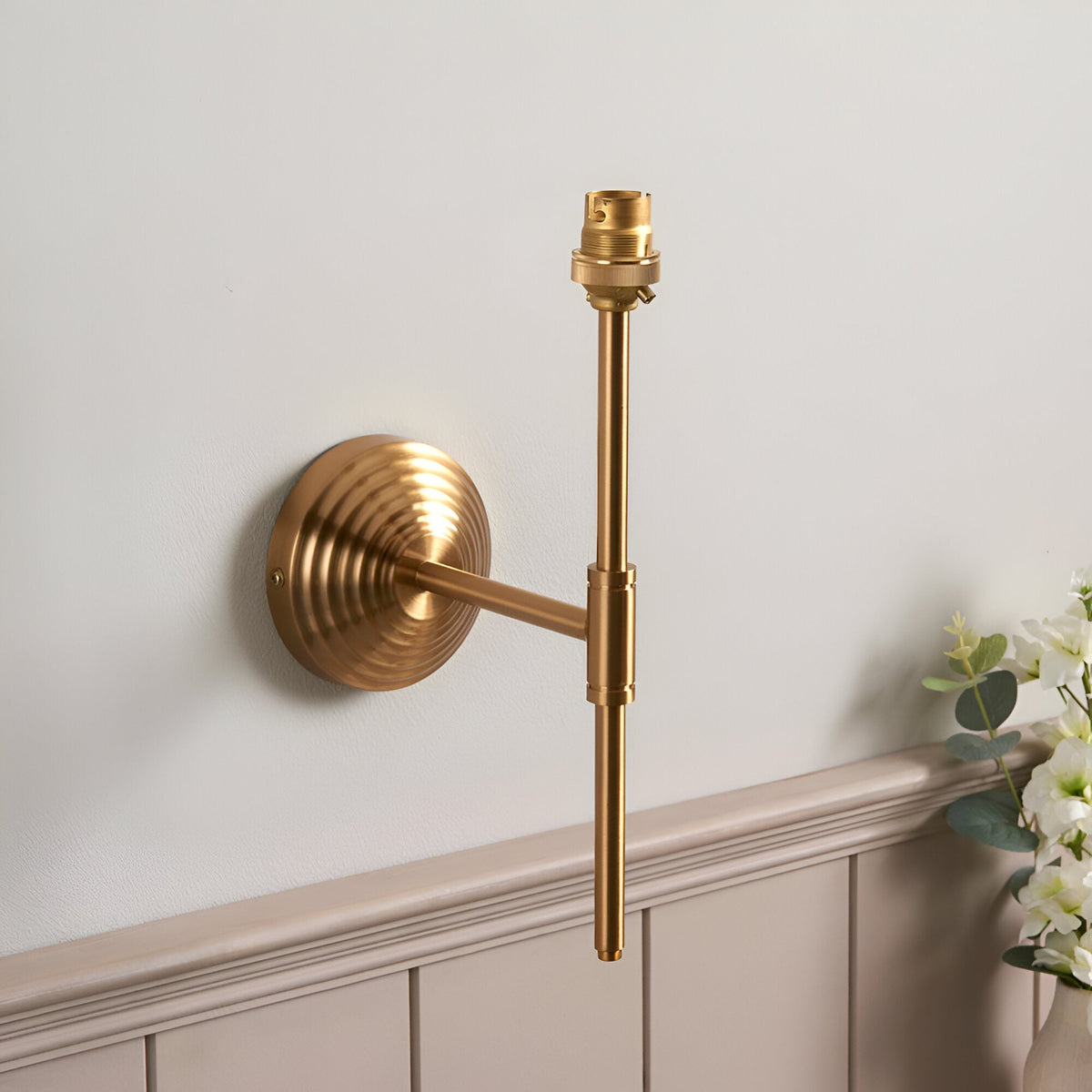 Endon Castleigh wall light in brushed aged brass with stepped back plate, adjustable T-shaped arm and B22 lampholder, shown shadeless on a pale wall.