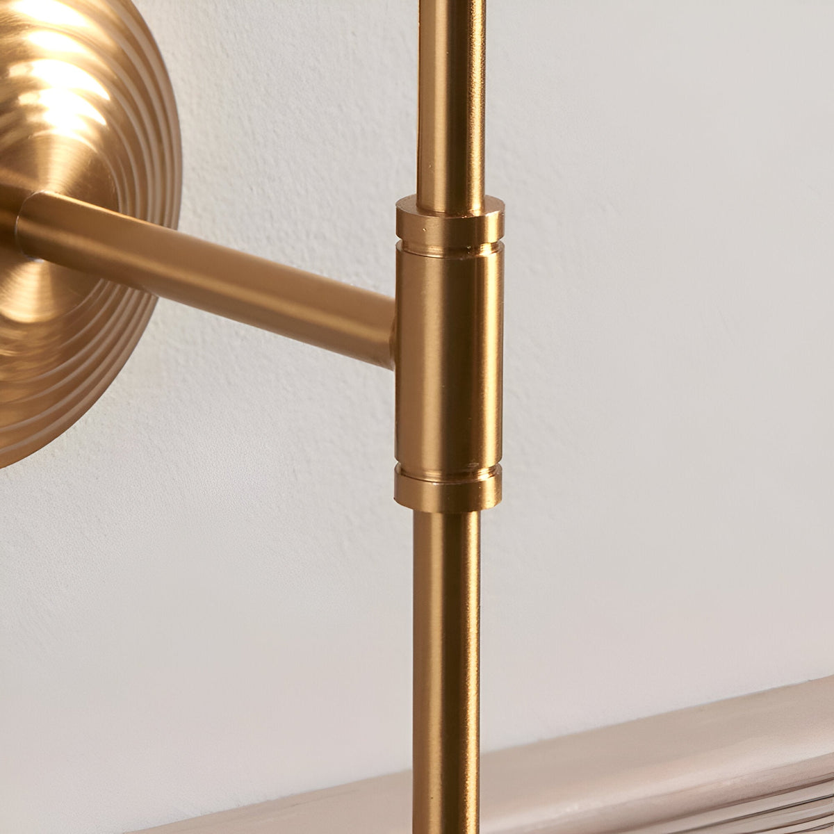 Close-up of the Endon Castleigh wall light showing the brushed aged brass stepped back plate, T-shaped adjustable arm and cylindrical joint detail.