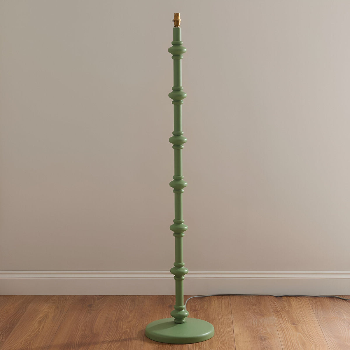 Endon Bevbury Ripple floor lamp base in Cotswold green with turned wooden spindle stem and brass B22 holder, shown on wood flooring against a neutral wall.