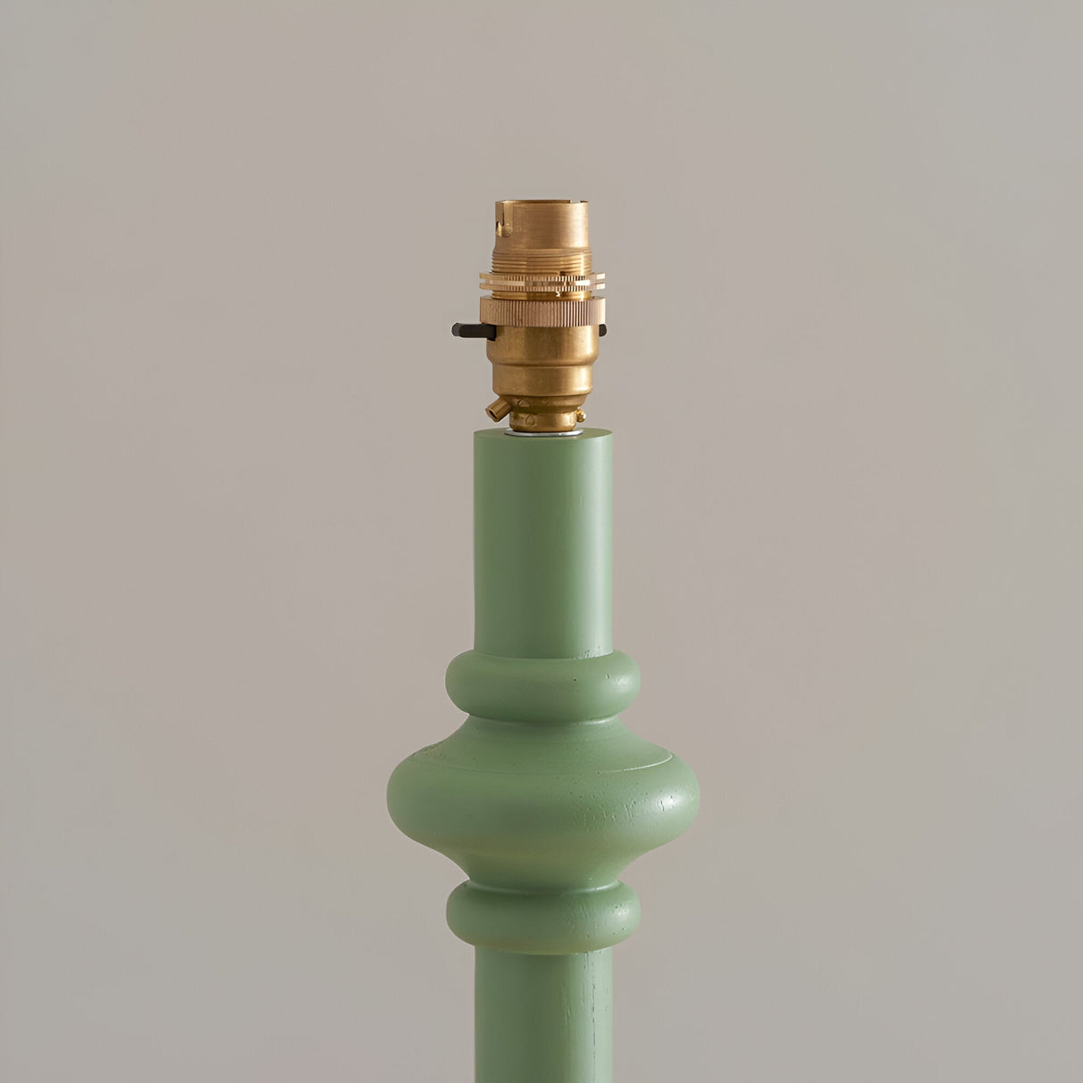 Close-up of the Endon Bevbury floor lamp's green turned wood spindle base with brass B22 switched lamp holder against a neutral background.