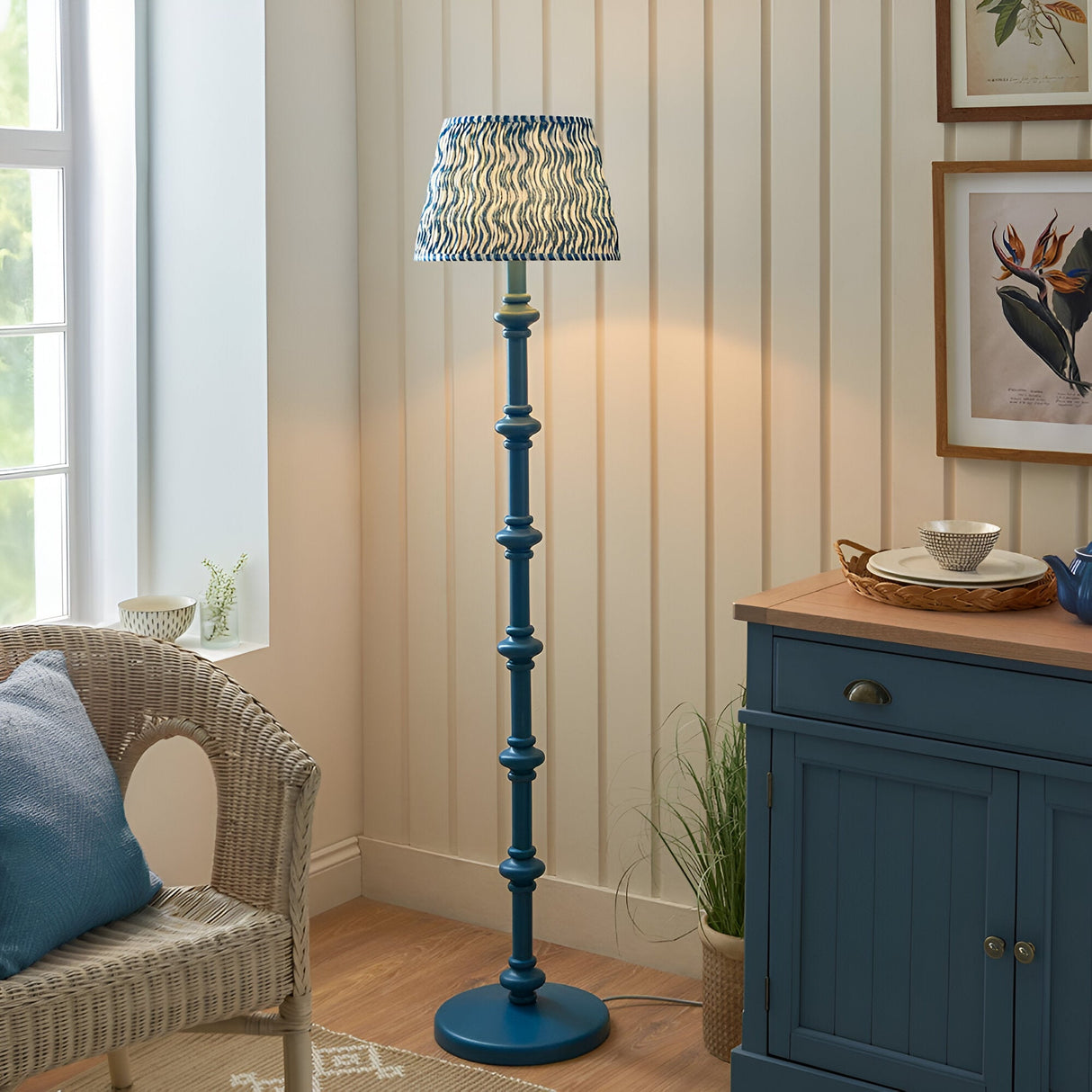Endon Bevbury Ripple floor lamp with blue turned wooden spindle base and blue wave-patterned tapered shade, in a cottage-style living room corner.