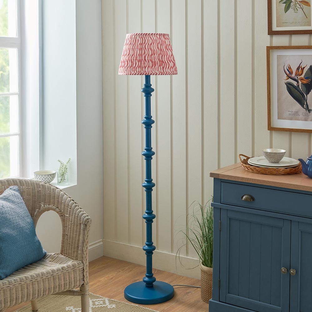 Endon Bevbury Ripple floor lamp with blue turned wood spindle base and pink patterned pleated shade, beside a rattan chair and blue sideboard.