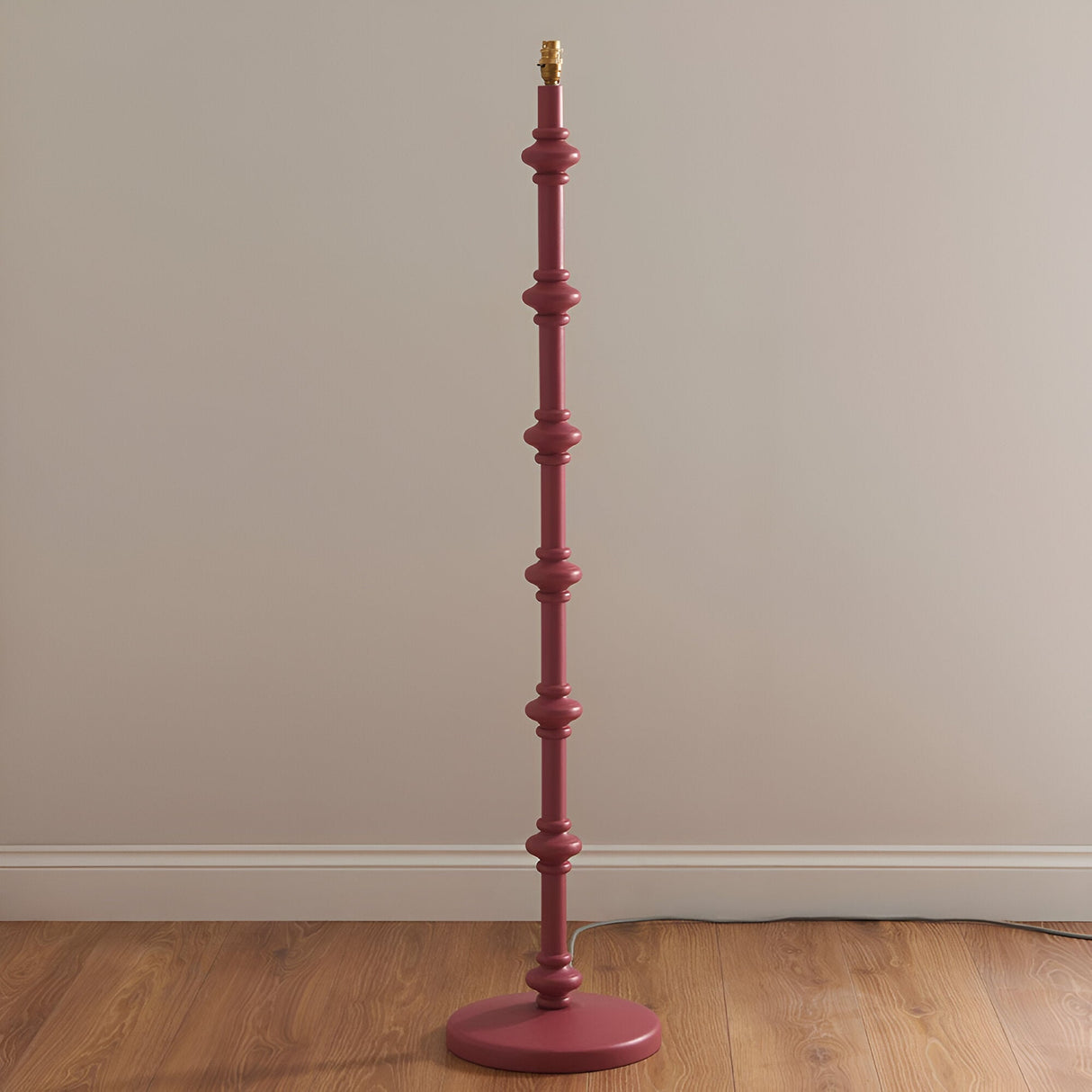Endon Bevbury Ripple floor lamp base in pink turned wood with spindle detailing and brass B22 holder, shown against a neutral wall on wooden flooring.