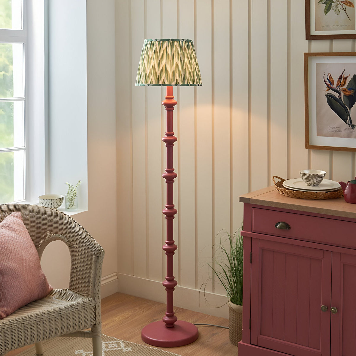 Endon Bevbury Zigzag floor lamp with pink turned wooden spindle base and green zigzag pleated shade, beside a wicker chair and pink sideboard.