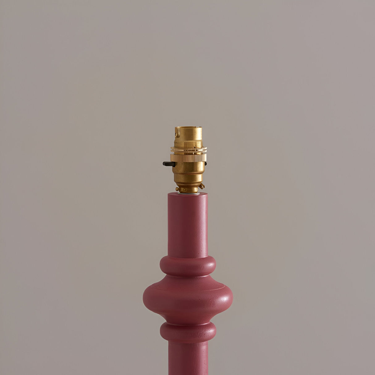 Close-up of the Endon Bevbury floor lamp's pink turned wood spindle base with switched brass B22 lamp holder, shown against a light neutral background.