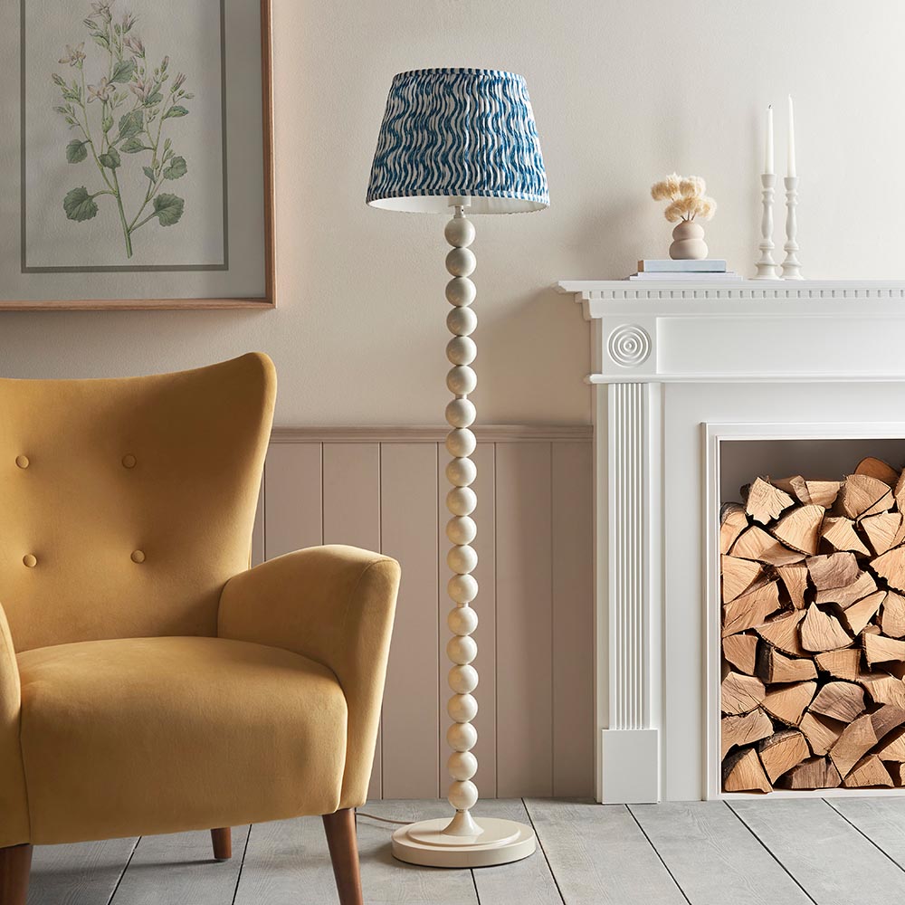 Endon Brenleigh Ripple floor lamp with stacked white sphere base and blue patterned faux linen shade, beside a yellow armchair and log-filled fireplace.