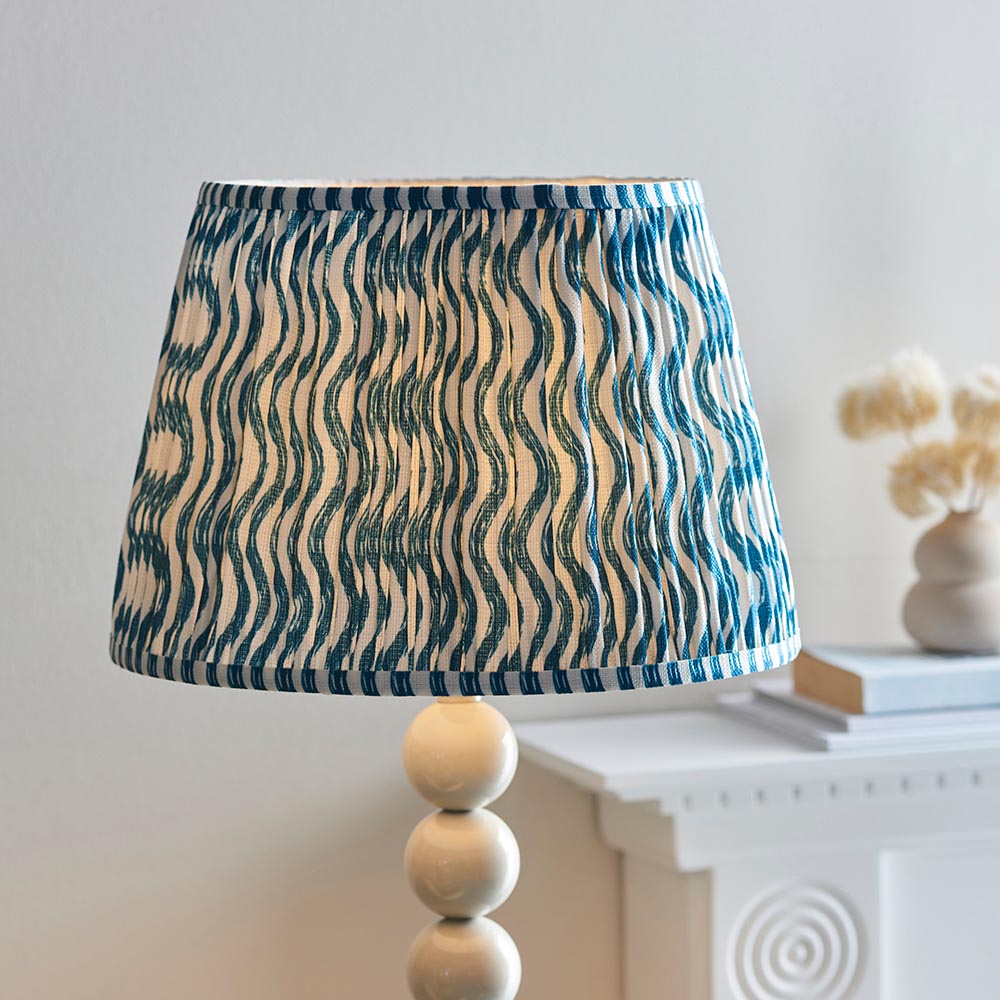 Endon Brenleigh Ripple floor lamp with a blue and white pleated faux linen shade on a glossy cream stacked sphere base, beside a mantelpiece.