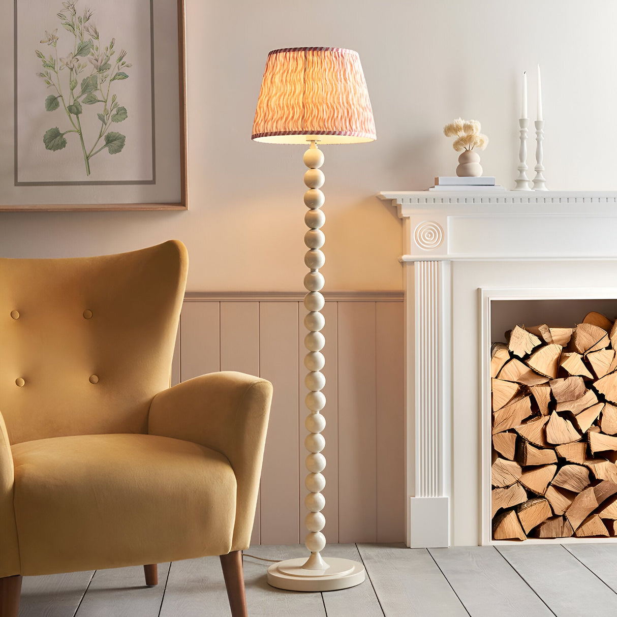 Endon Brenleigh floor lamp with stacked white sphere base and pink Ripple pleated shade, beside a mustard armchair and white fireplace with logs.