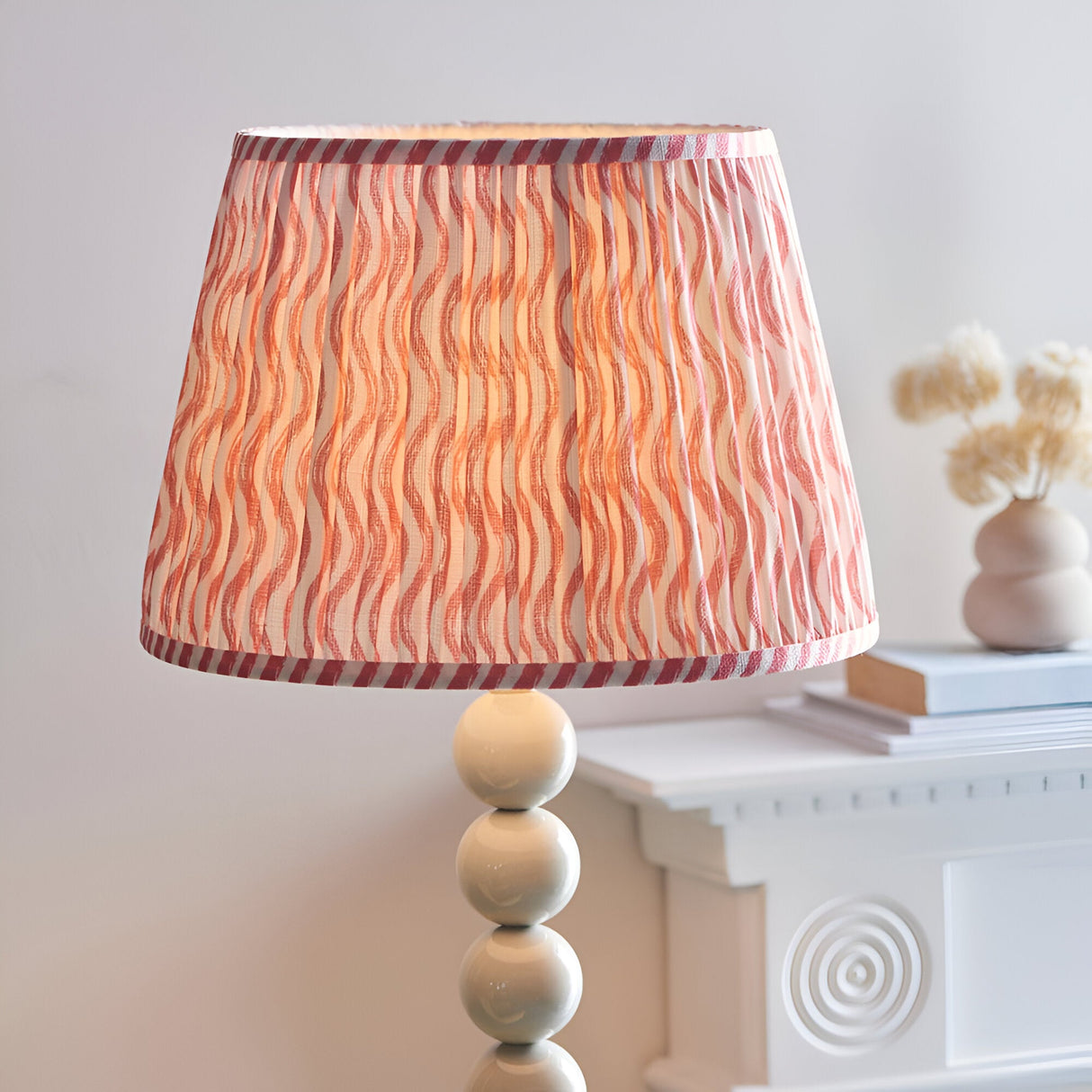 Endon Brenleigh Ripple floor lamp with a pleated white and pink wavy patterned shade on a glossy cream stacked sphere base beside a white mantel.