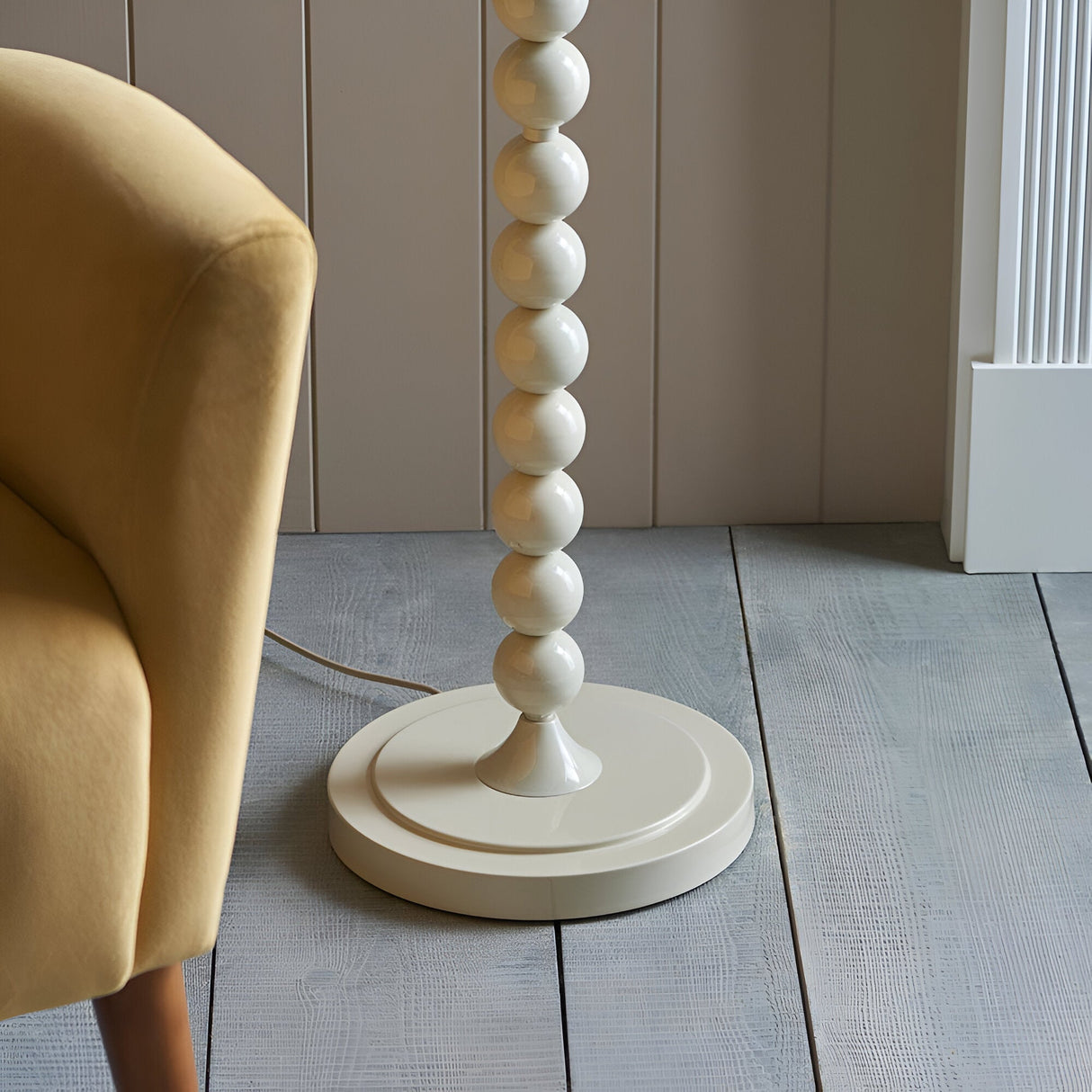 Endon Brenleigh floor lamp base with glossy white stacked spheres on a round base, beside a mustard velvet chair on grey plank flooring.