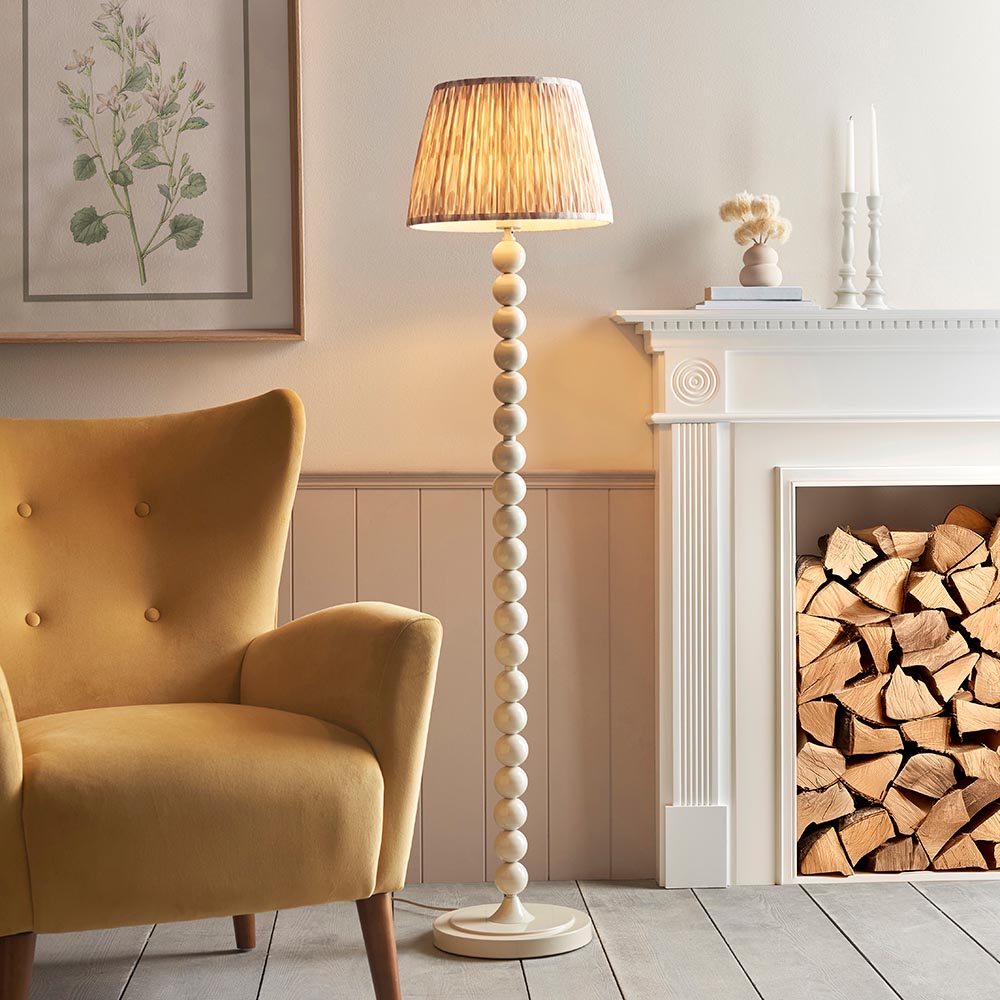 Endon Brenleigh stacked sphere floor lamp in white with a natural Ikat pleated shade, beside a mustard velvet armchair and white fireplace with logs.