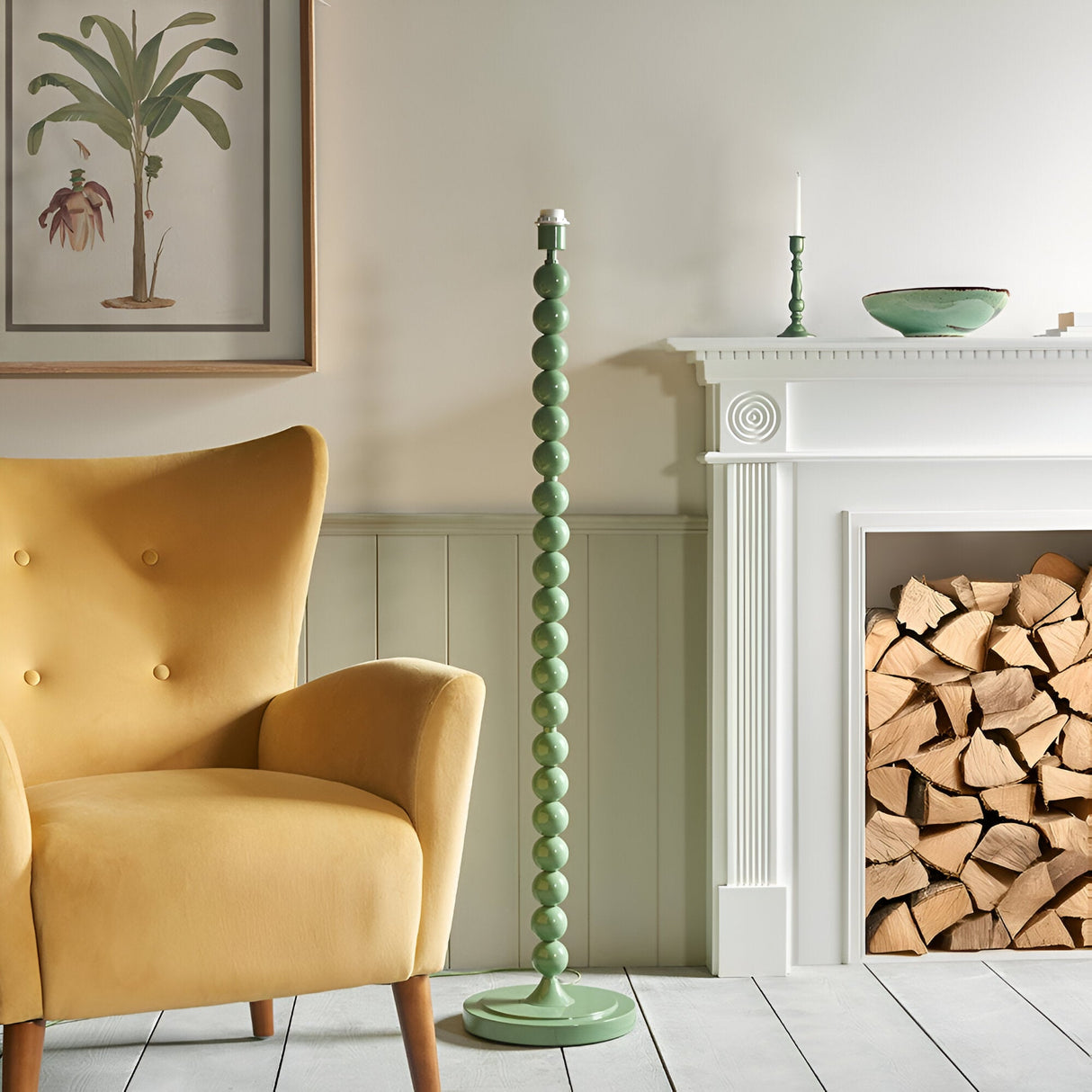 Endon Brenleigh green stacked sphere floor lamp without shade beside a yellow armchair and white fireplace with stacked logs in a living room.