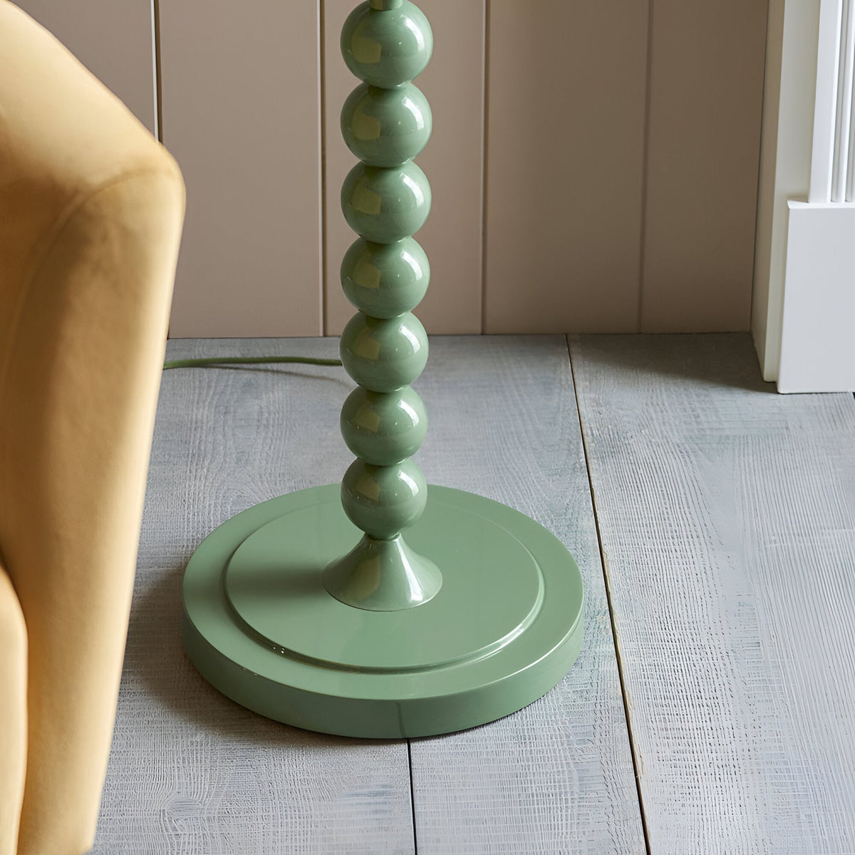 Close-up of the Endon Brenleigh Ripple floor lamp base, showing stacked green gloss spheres on a round base beside a mustard chair on pale wood flooring.