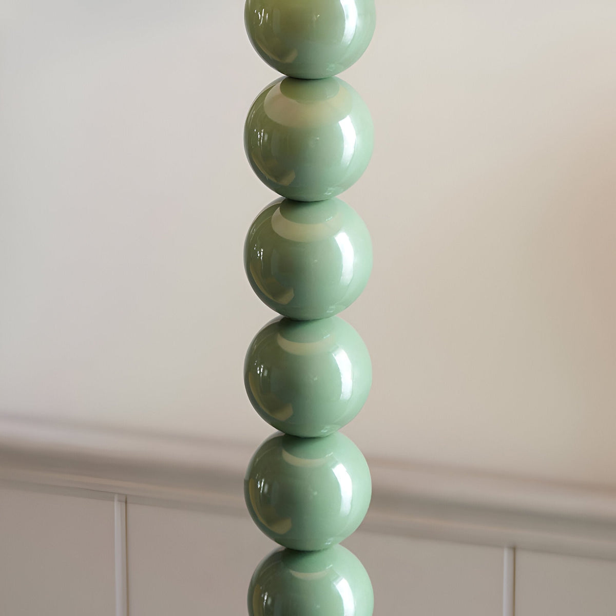 Close-up of the Endon Brenleigh Ivy floor lamp base showing stacked glossy Cotswold green metal spheres against a neutral panelled wall.