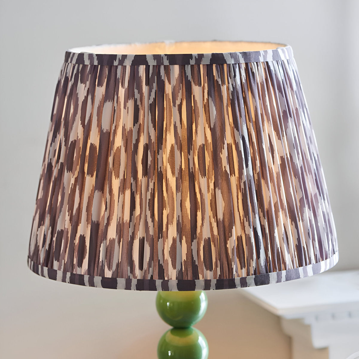 Endon Brenleigh floor lamp shade in grey Ikat pleated faux silk, set on a glossy green stacked sphere base beside a pale side table.