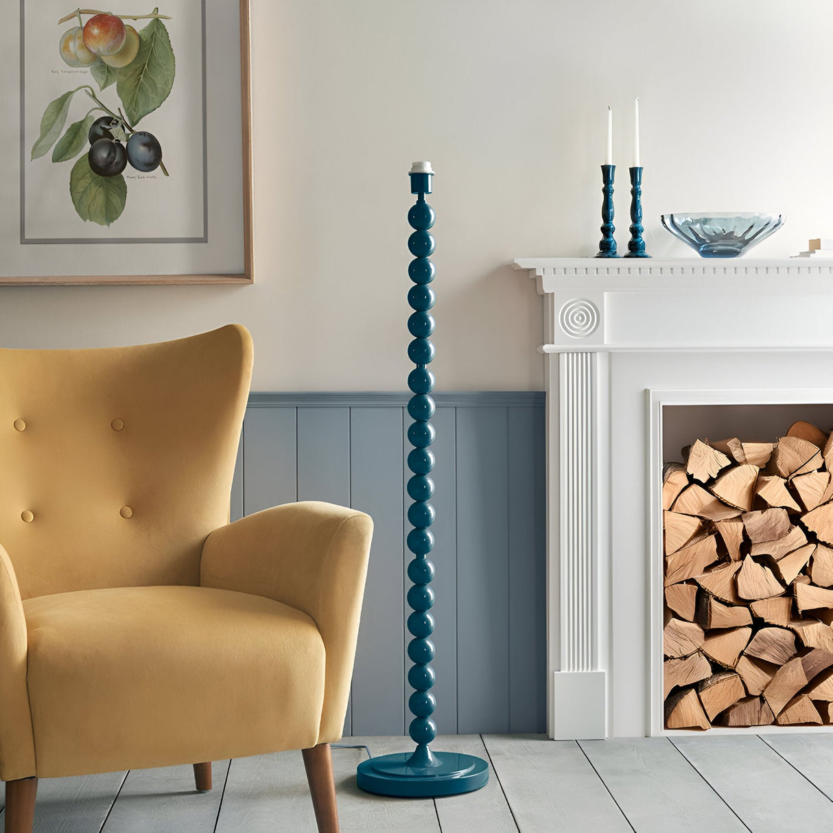 Brenleigh Ivy floor lamp with stacked sphere metal base in teal blue, shown without shade in a living room beside a yellow armchair and fireplace.