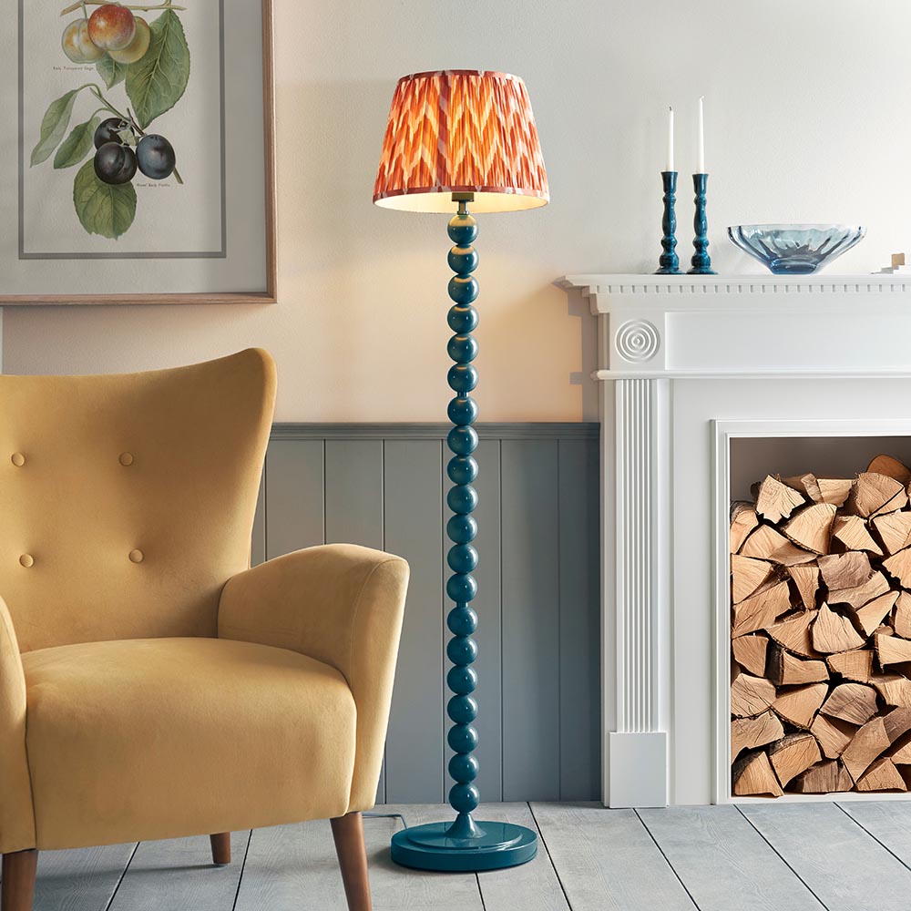 Endon Brenleigh stacked sphere floor lamp in glossy marlin blue with a pleated Zigzag shade, beside a mustard armchair and white fireplace with logs.
