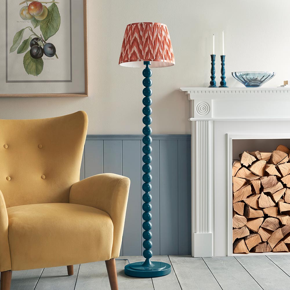 Endon Brenleigh Zigzag floor lamp in marlin blue with stacked sphere metal base and pleated pink zigzag shade, beside a yellow armchair and fireplace.