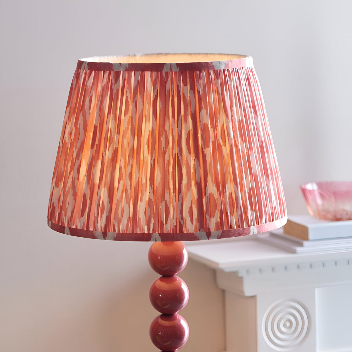 Endon Brenleigh floor lamp with pink stacked sphere base and pleated Ikat faux silk shade in pink and coral tones, beside a white mantel.