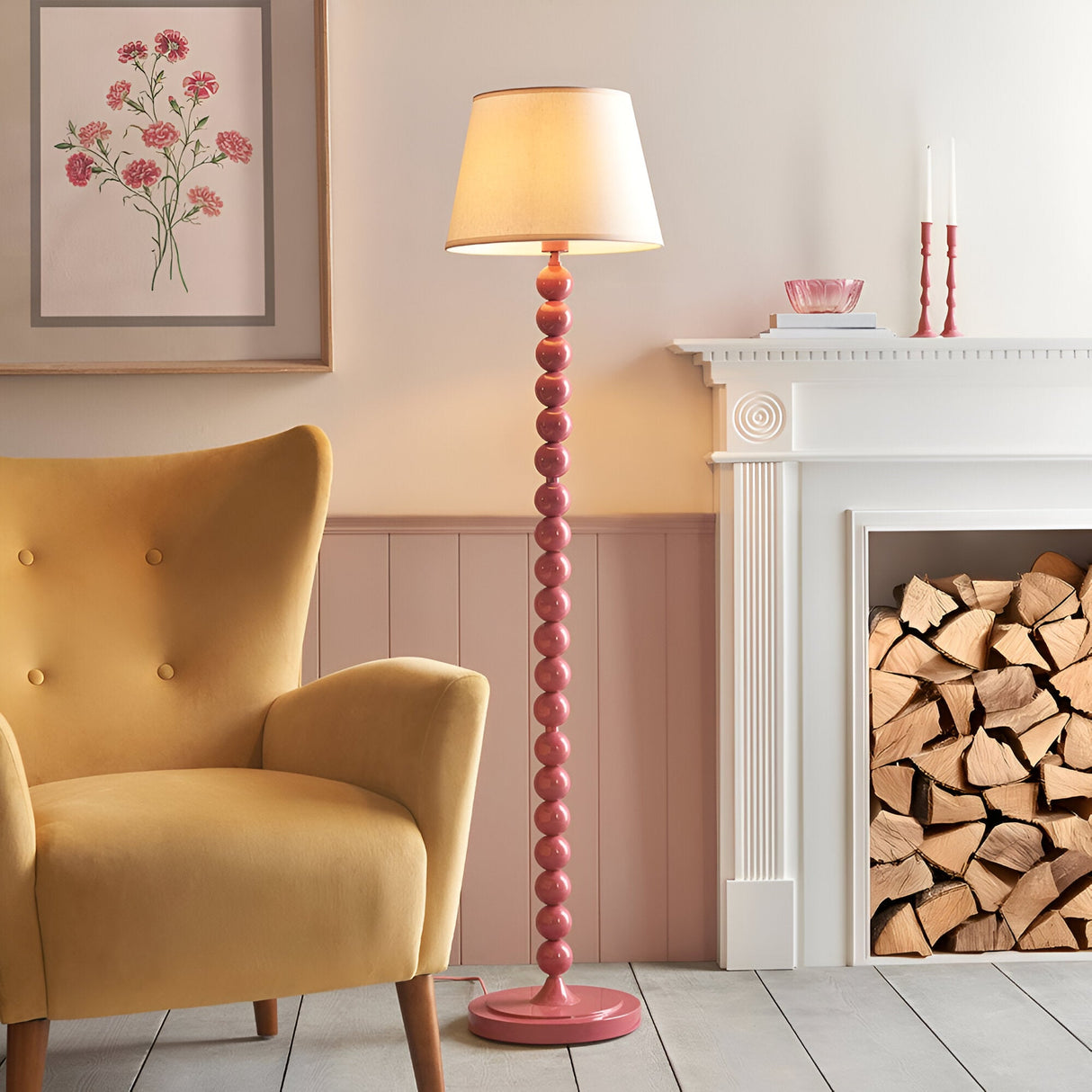 Endon Brenleigh Ivy floor lamp with stacked pink gloss sphere base and white tapered shade, beside a mustard armchair and white fireplace with logs.