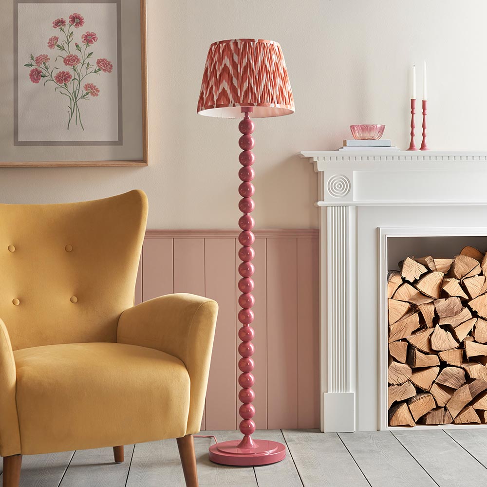 Brenleigh Zigzag Floor Lamp in pink with stacked sphere base and pleated zigzag-print shade, shown beside a fireplace in a living room setting.
