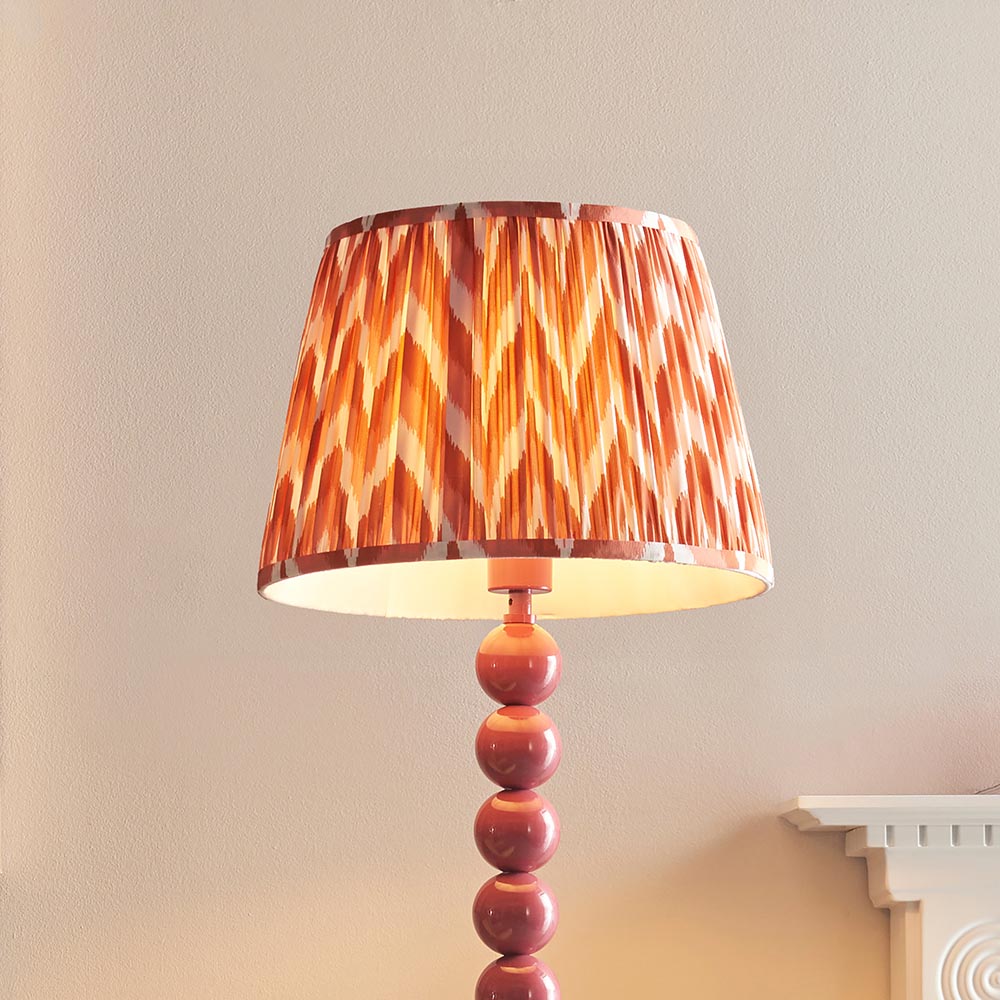 Brenleigh Zigzag Floor Lamp with pink stacked sphere base and orange chevron pleated fabric shade, shown against a light wall.