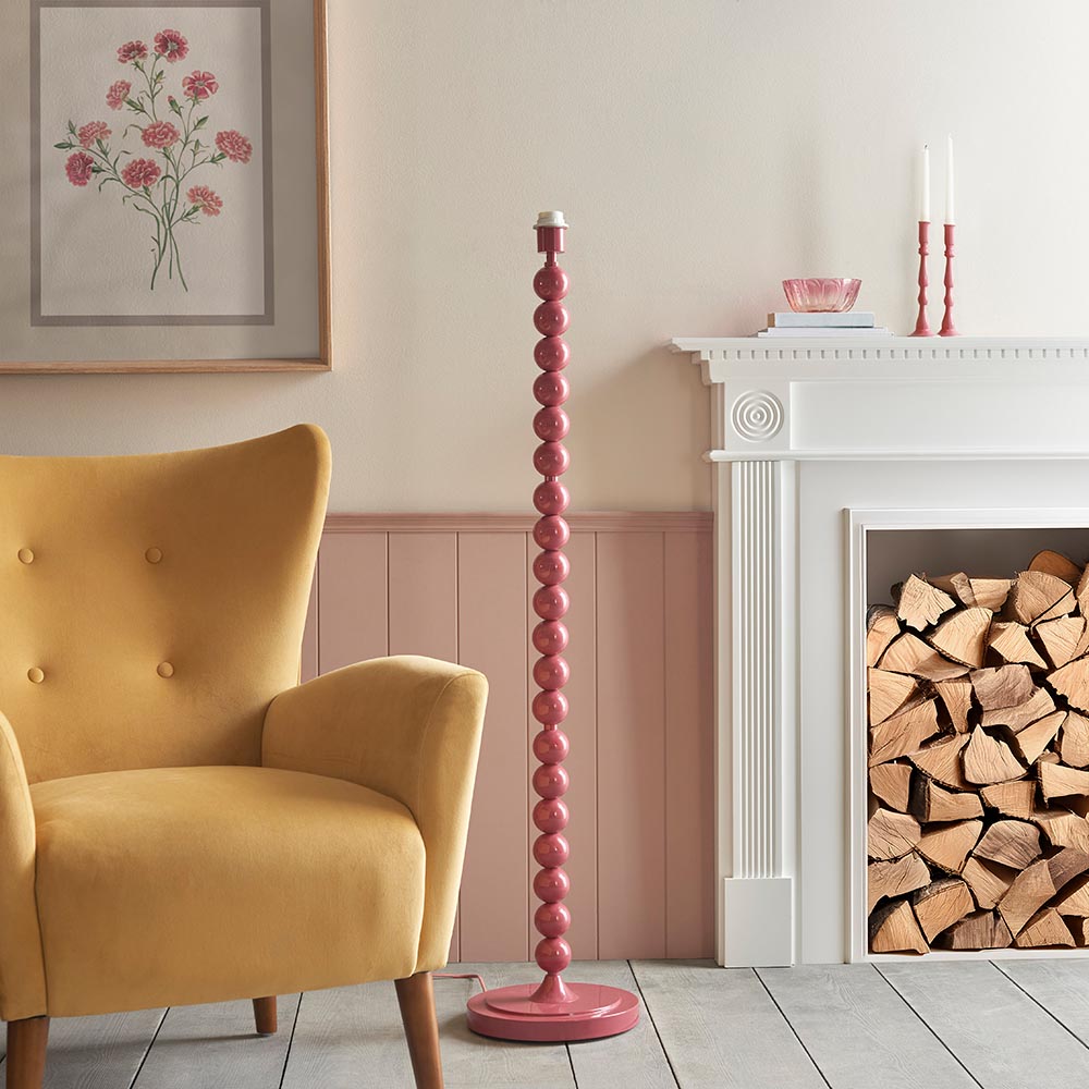 Brenleigh Zigzag Floor Lamp in pink with stacked sphere metal base, shown unshaded beside a fireplace and mustard armchair in a living room.