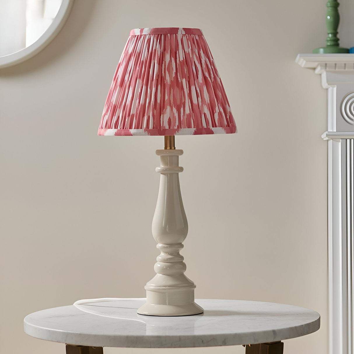 Endon Carlworth Ikat table lamp in almond gloss resin spindle base with pleated coral and white Ikat shade, on a marble side table by a mirror.