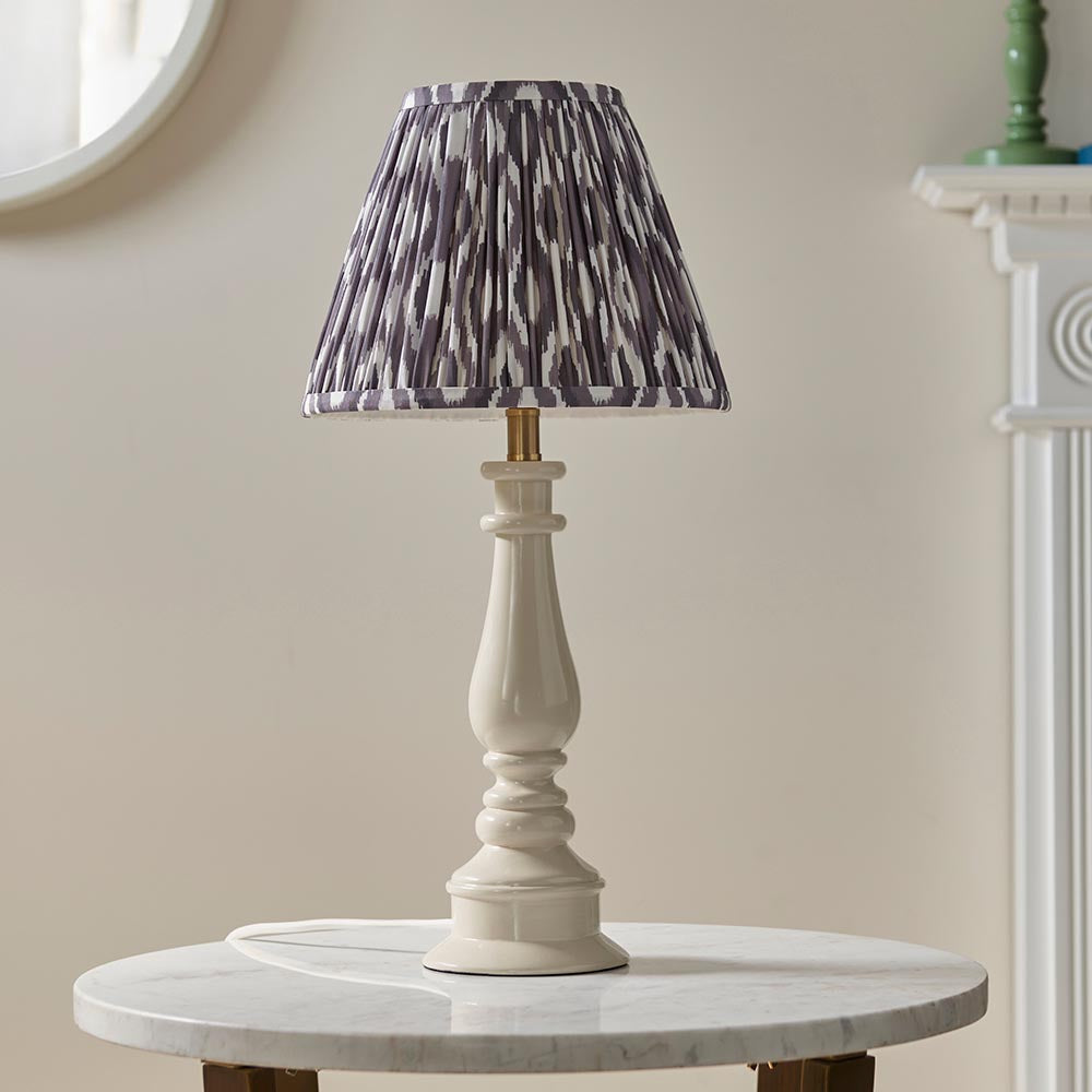 Endon Carlworth Ikat table lamp with an almond gloss resin spindle base and grey pleated Ikat shade on a marble table beside a round mirror.