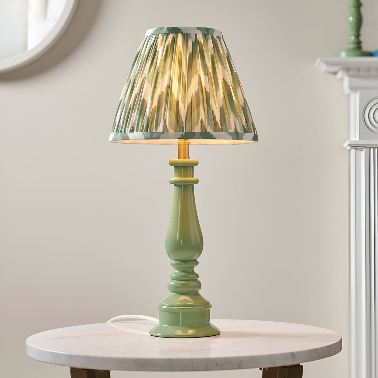 Carlworth Zigzag Table Lamp with green resin spindle base and pleated green zigzag-patterned shade, shown lit on a marble side table.