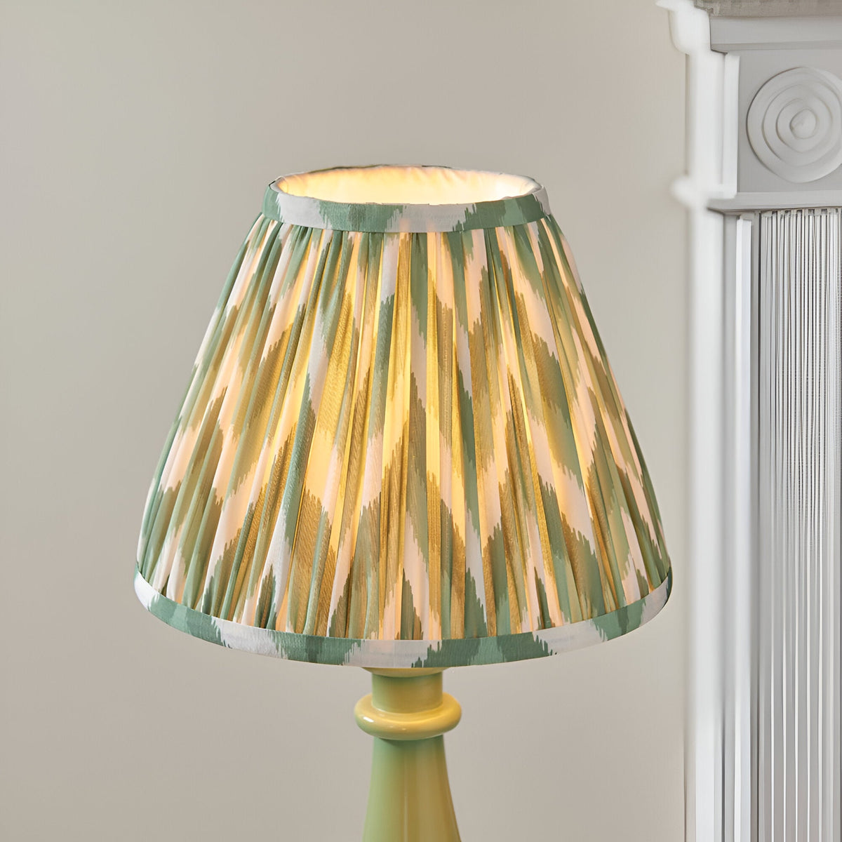 Carlworth Zigzag Table Lamp with pleated green, cream and gold patterned shade on a glossy green spindle-style resin base, set against a light background.