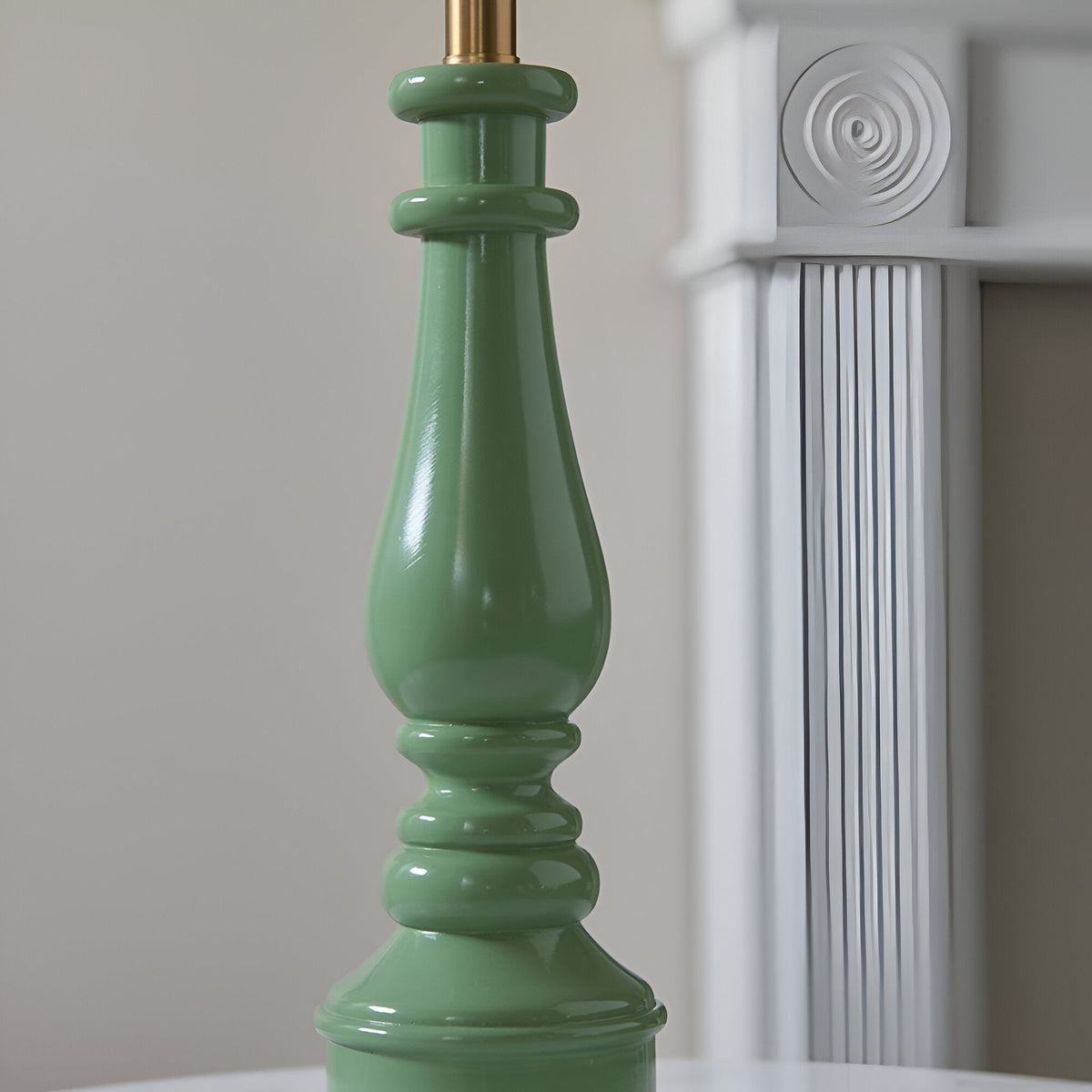 Close-up of the Endon Carlworth Ivy table lamp's turned green resin spindle base with brass lamp holder, beside a white fluted column.