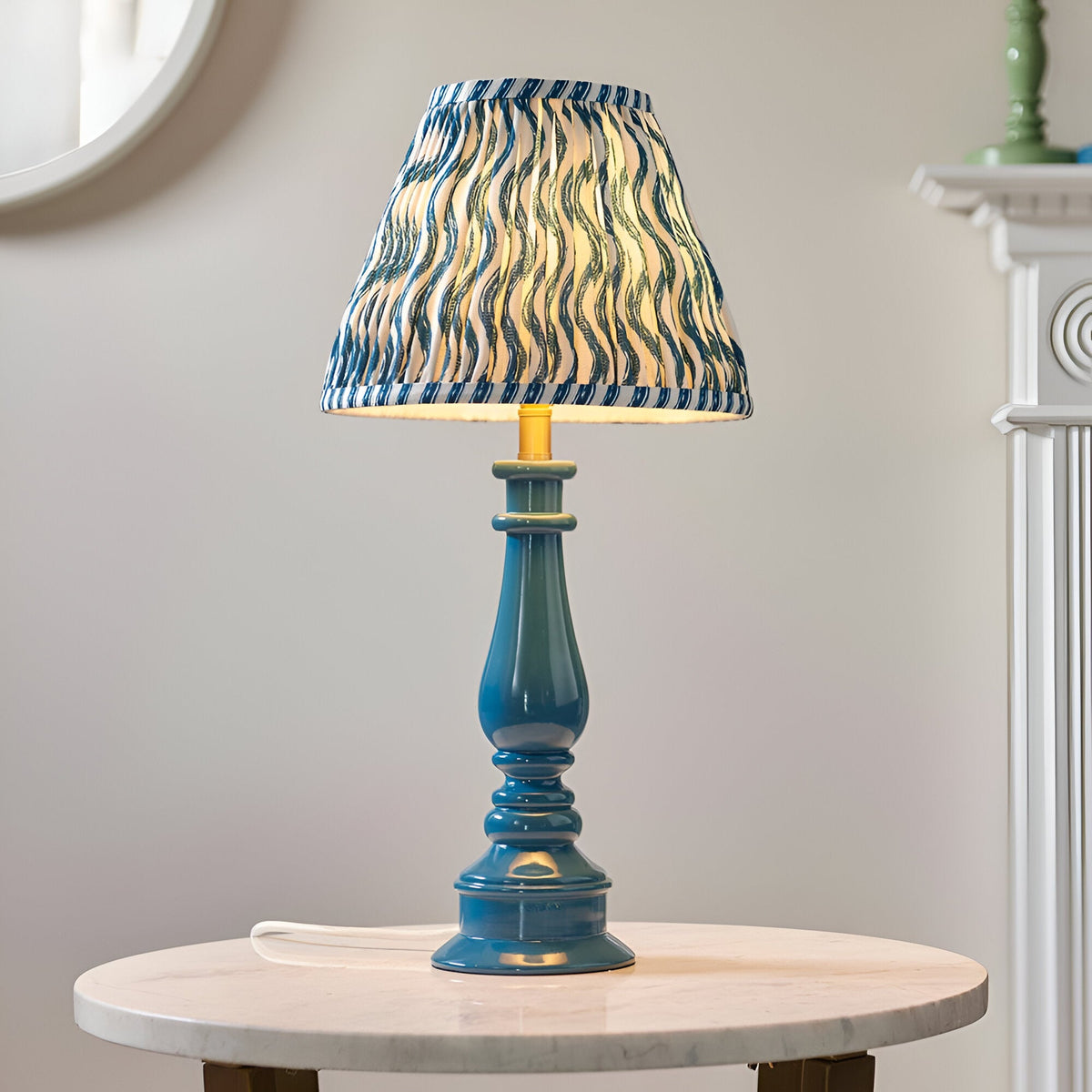 Carlworth Ripple Table Lamp in glossy blue resin with turned spindle base and pleated blue patterned fabric shade, shown on a marble side table.