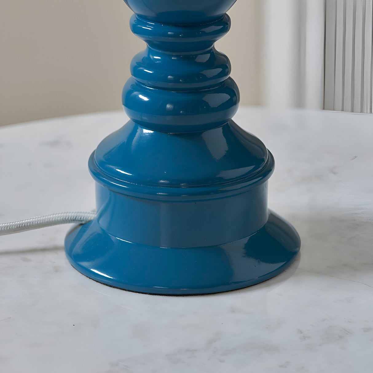 Close-up of the Carlworth Ripple Table Lamp base in glossy marlin blue resin with ripple detailing, on a marble surface with pale braided flex.