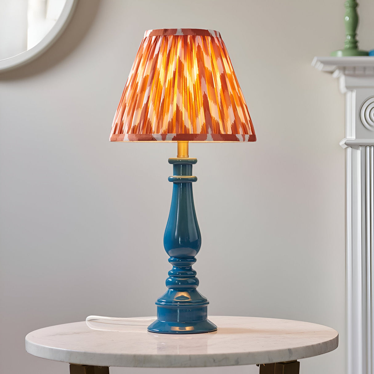 Endon Carlworth table lamp with marlin blue turned resin spindle base and pleated apricot zigzag shade, lit on a marble side table.