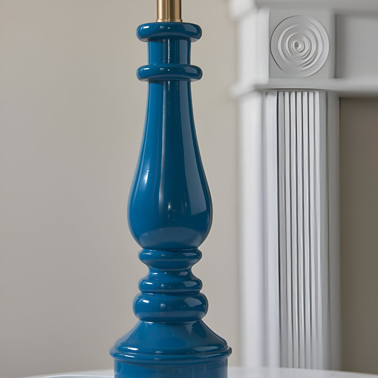 Close-up of the Endon Carlworth Ivy table lamp's high gloss marlin blue turned resin spindle base with brass fitting, beside a white fluted column.