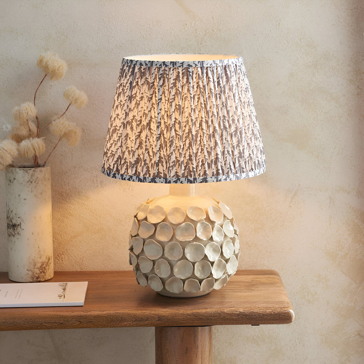 Ashbury Leaf Table Lamp with round textured ceramic base and pleated grey leaf-print fabric shade, styled on a wooden console table.