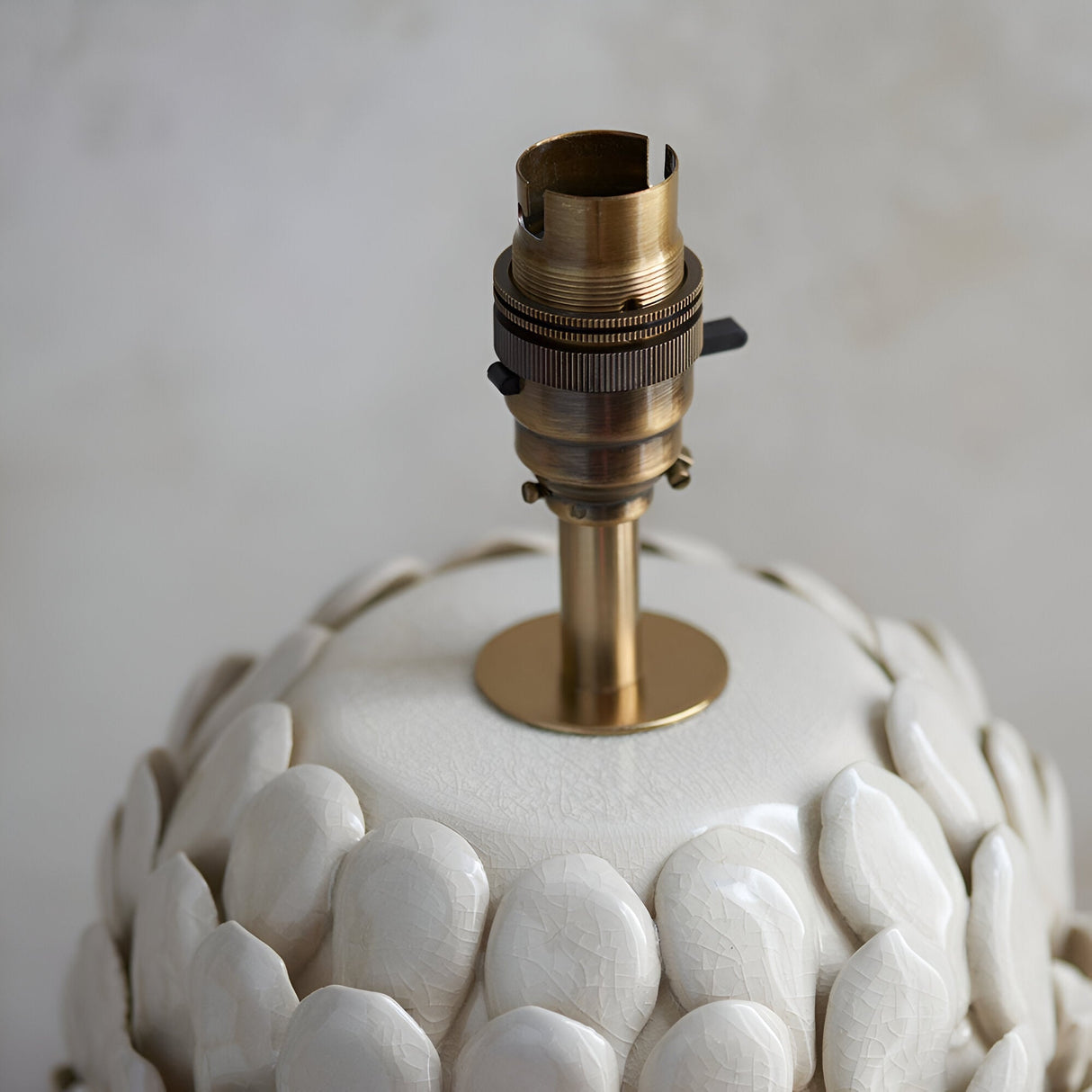 Close-up of the Caldford Ivy table lamp base showing an antique brass B22 lamp holder and stem atop a white ceramic crackle-glazed leaf-textured base.